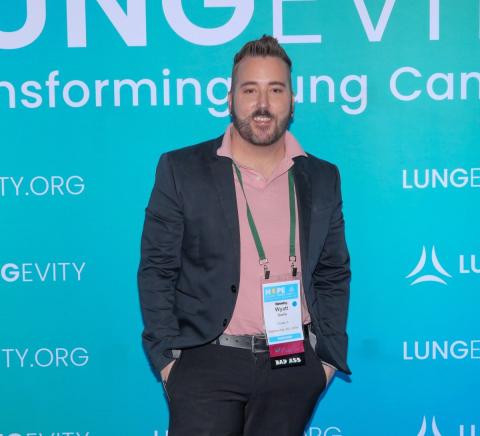 Wyatt in front of a lungevity hope summit banner smiling in a casual suit